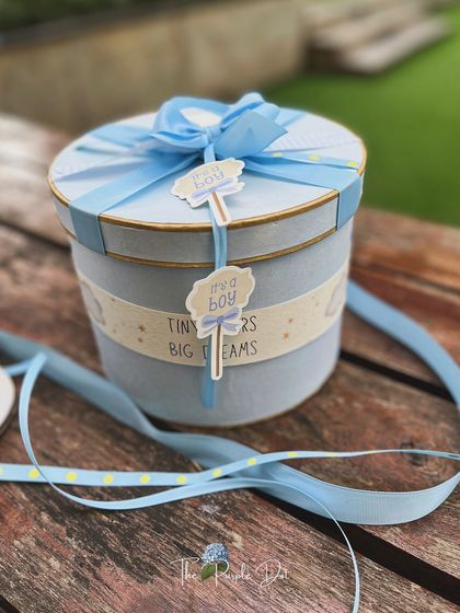 A full view of the round keepsake box, elegantly wrapped to welcome a baby boy. The soft blue color and layered ribbons make it a beautiful statement piece.