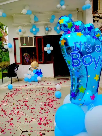 Announce his arrival with a big statement! This outdoor welcome decoration features a large "It's a Boy!" foot-shaped foil balloon, blue and white balloon columns, and a pathway sprinkled with fresh flower petals.