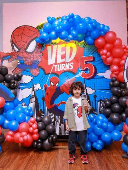 The birthday boy stands proudly in front of his amazing Spider-Man 5th birthday backdrop, complete with a cityscape, balloon arch, and multiple Spidey cutouts.