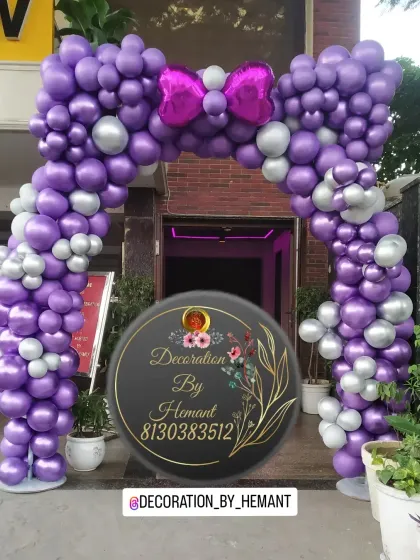 A grand entrance arch made of purple and silver balloons, topped with a large pink foil bow. This type of arch makes a bold statement at the entrance of any party venue.