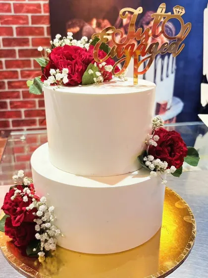 A simple yet beautiful two-tier engagement cake. The clean white fondant is the perfect canvas for the fresh red carnations and the custom "Just Engaged" topper.