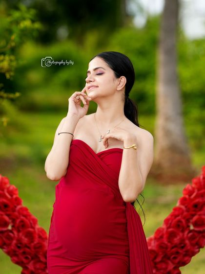 A close-up portrait of a glowing mother-to-be in a red gown, framed by our red floral heart prop.