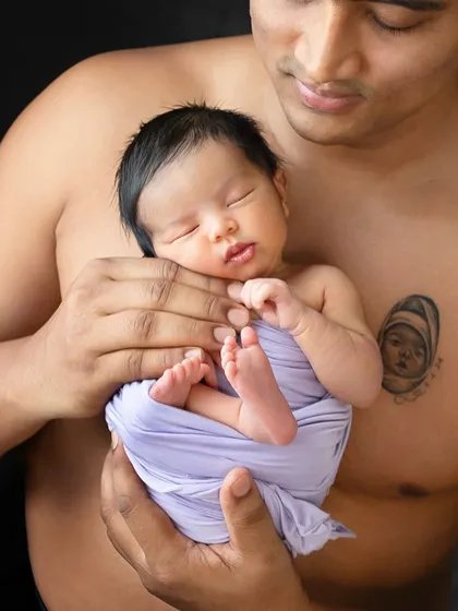 A new dad holds his sleeping baby, her tiny body wrapped in purple. These quiet moments of connection remind us how fleeting and precious the newborn phase is.