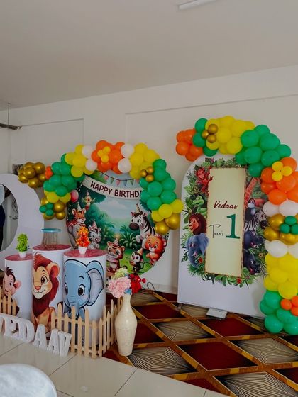 A classic jungle book style setup for a first birthday. It includes a circular backdrop with cartoon animals, character-themed pedestals, and a colorful balloon arch.