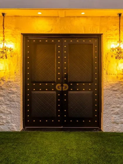 The entrance to the Gallops banquet hall sets the stage for the elegance within. The grand, studded black doors are flanked by classic chandeliers against a textured white stone wall. This design creates a dramatic and welcoming entry, promising a memorable experience for every guest.