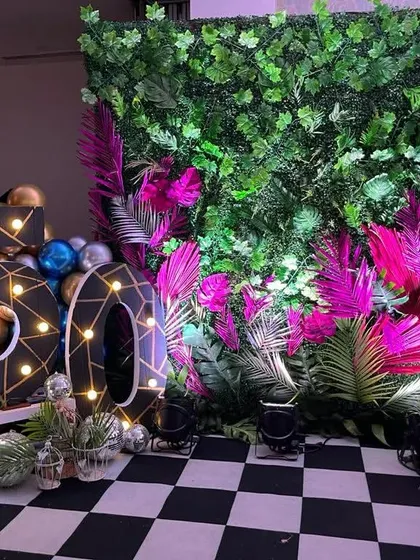 A unique 50th birthday decoration with a checkerboard floor. The setup includes a lush green wall with pink accents and large, stylish marquee numbers.