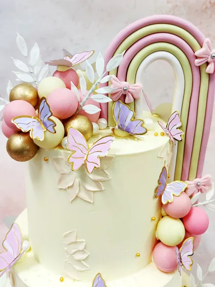 A close-up of our two-tier Rainbow Butterfly Cake, showcasing the soft pastel rainbow, delicate butterflies, and elegant white foliage.