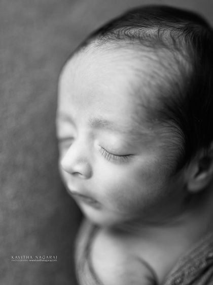 A nine-day-old newborn, captured in a simple, elegant black and white portrait. The focus is on their sleepy, curled-up form, a fleeting moment preserved forever.
