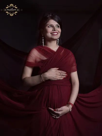 A radiant mother-to-be in a flowing dark red gown against a dramatic backdrop. Our studio maternity sessions are designed to make you feel like a star, capturing your pregnancy glow.