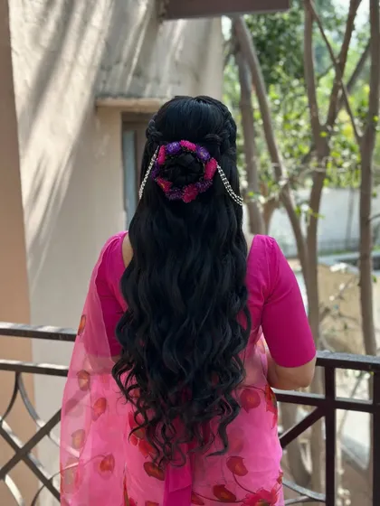 A unique half-up, half-down style for a haldi ceremony, featuring a bun made of colorful fabric and chain accessories, with long, crimped waves cascading down.