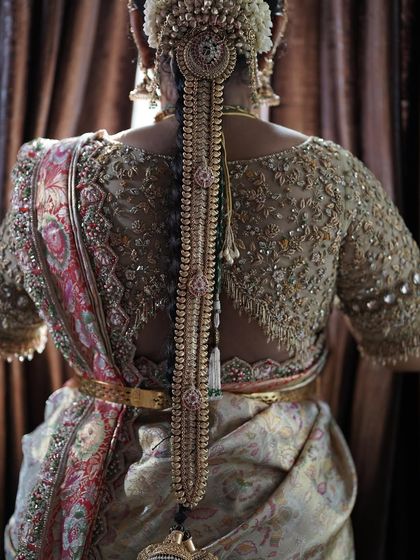 The back of a bridal blouse, a canvas of intricate gold embroidery and beadwork. The design is perfectly symmetrical, framing the bride's traditional hairstyle and jewelry.