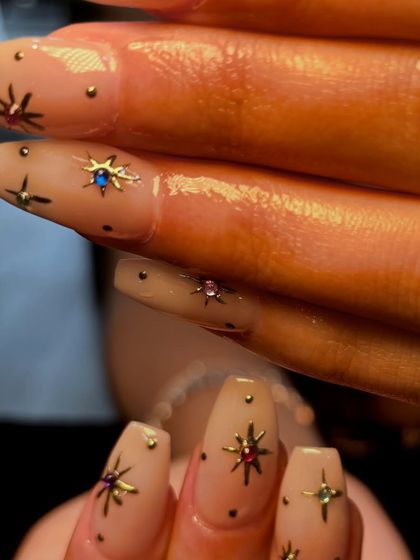 A macro shot of the celestial-themed nail art, detailing the tiny, colorful rhinestones placed in the center of the metallic stars.