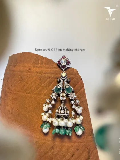 This chandelier earring combines polki diamonds, pearls, and emerald drops in a traditional jhumka-inspired design. It's a blessing in gold for any festive occasion.