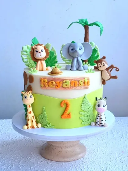 A single-tier jungle animal cake, perfect for a smaller celebration. It features adorable, hand-sculpted fondant animals like a lion, elephant, monkey, giraffe, and zebra.