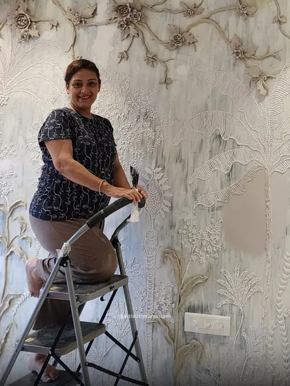 Here I am, working on a large, nature-inspired mural. The piece features a variety of sculpted plants and flowers, creating a rich tapestry of textures that brings the wall to life.