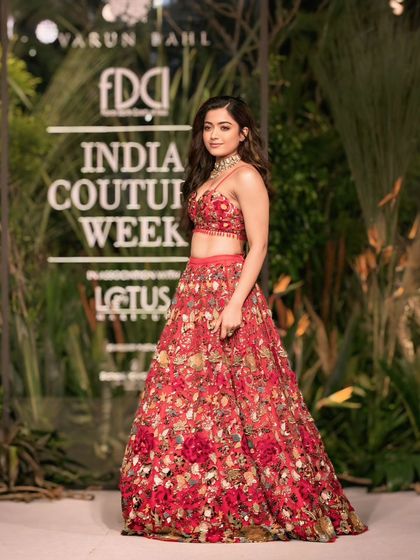 A full-length shot of Rashmika Mandanna posing in front of the India Couture Week backdrop. This is a key shot for event branding and media coverage.