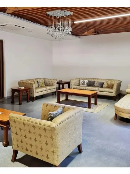 A formal living room setup with classic upholstered sofas and a crystal chandelier, contrasted with a modern wooden false ceiling.
