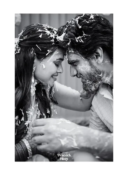 An intimate moment from a Haldi ceremony, captured in soft black and white. The focus is entirely on the couple's tender connection, their foreheads touching amidst the playful mess.