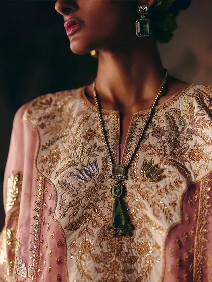 A close-up of a similar piece, highlighting the rich, intricate gold and silver embroidery on the yoke, paired with a striking green pendant necklace.