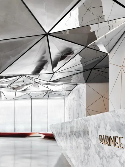 The reception desk and its reflection, showcasing the precision of the design and the immersive quality of the space. The logo is subtly integrated into the overall geometric theme.