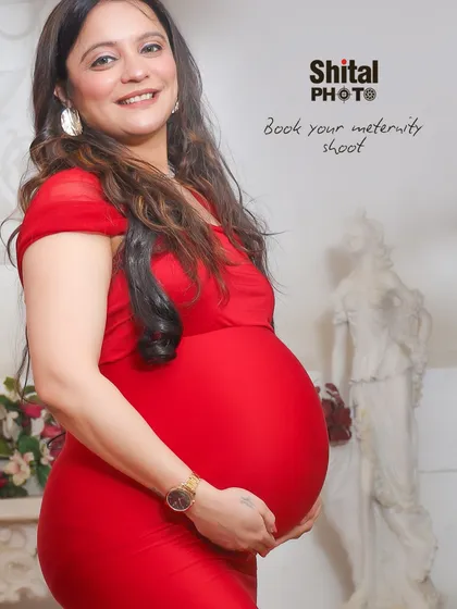 A close-up shot focusing on the beautiful baby bump. The mom-to-be's smile and the vibrant red of her dress make this a joyful and warm maternity portrait.