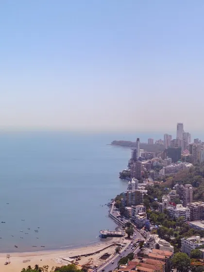 A sweeping drone shot looking down the coastline from Malabar Hill, showing the curve of the bay and the city stretching into the distance.
