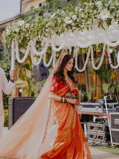 The bride's elegant entry, holding a bouquet of red roses. Her long, flowing veil and simple makeup create a look of timeless grace.
