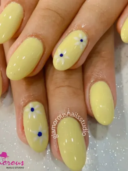 A simple and sweet design of pastel yellow nails with accent nails featuring small, hand-painted white daisies.