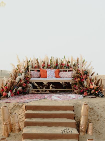 The bride's seating for the desert Mehendi, set against an arch of pampas grass and florals. Carved into the sand, this spot was designed to be a natural and beautiful focal point for the ceremony.