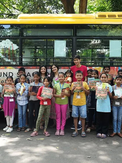A group photo of the children and our team in front of the 'Sound Space on Wheels' bus, proudly holding their new books.