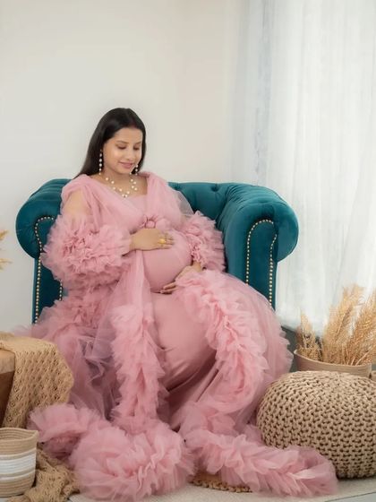A serene portrait of a mom-to-be in a flowing pink gown, seated in my studio's lifestyle corner. The soft, natural light and boho decor create a peaceful and dreamy atmosphere.