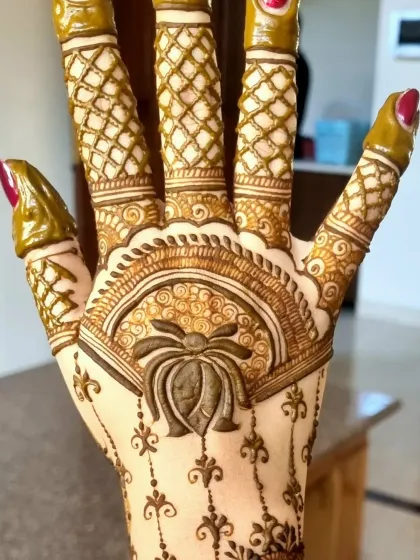 This design focuses on the back of the hand, featuring a large lotus motif. The fingers are decorated with a net pattern, a classic element in many henna styles.