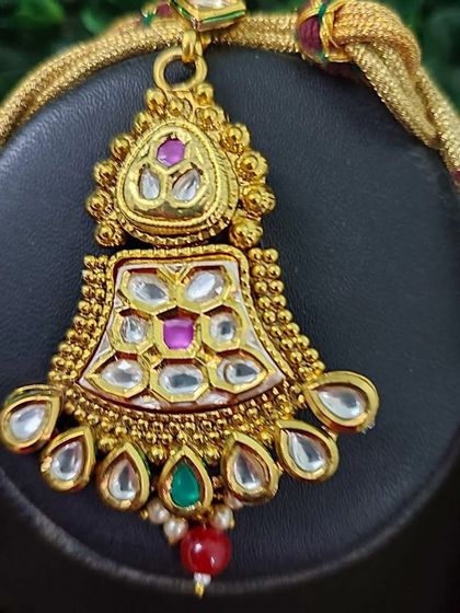 A close-up of the maang tikka from the bridal set with deep magenta beads. The piece features kundan work with pink and green accents.