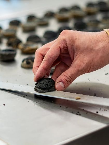 Precision in every detail. A chef carefully places a dark, textured garnish onto a pastry, showcasing the meticulous handwork that goes into our dessert creations.