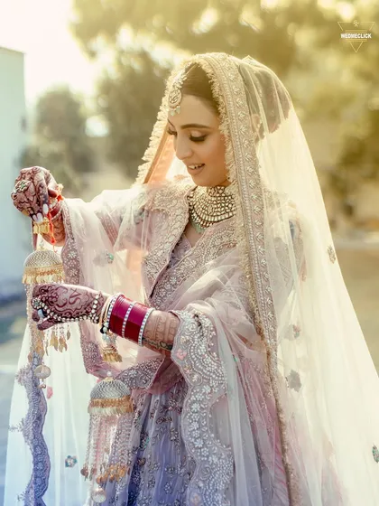 A stunning shot of the bride playing with her kalire, the sunlight catching the intricate details of her jewelry and veil.