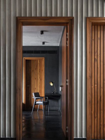 A view through doorways in the Brick House reveals layers of texture, from fluted concrete walls to ribbed wooden doors, creating a rich and cohesive material palette.