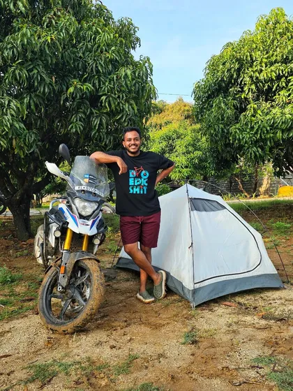 The adventure doesn't stop when the engines turn off. A rider relaxes by his tent and his mud-splattered BMW GS 310 after a full day of training, ready for a night of camping with the crew.