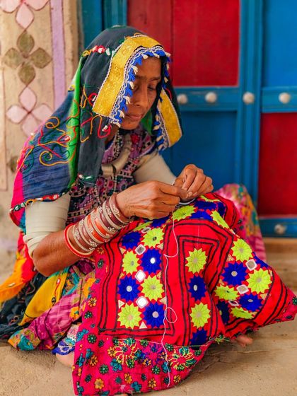 A close-up shot of a Meghwal woman's hands as she works on a piece of traditional embroidery. The vibrant colors and mirror work are characteristic of the tribe's artistry.