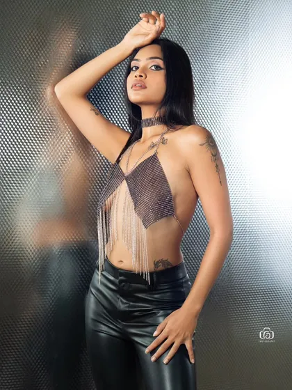 This portrait captures a modern, edgy aesthetic with a chainmail top and leather pants. The lighting is focused to create a slight motion blur effect, adding a dynamic quality to the studio shot.