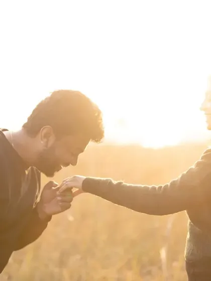 A chivalrous and romantic gesture. He gently kisses her hand in the middle of a sun-drenched field, a timeless expression of love and adoration.