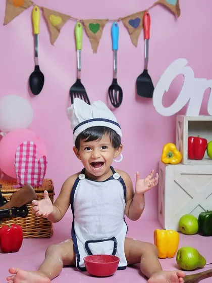 This little chef is ready to get messy. The setup is complete with a chef's hat, apron, and plenty of colorful props before the cake smash begins.
