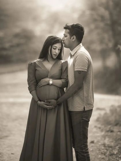 A black and white version of a tender couple's portrait outdoors. The focus is on the husband's gentle kiss on his wife's forehead, a classic expression of love and protection.
