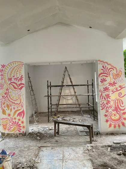This is 'Baba's Garden,' a mural I painted in Amritsar. The project was a challenge after an elbow injury, but I was determined to bring this vision to life. The design features ethnic floral and bird motifs in warm pink and gold.