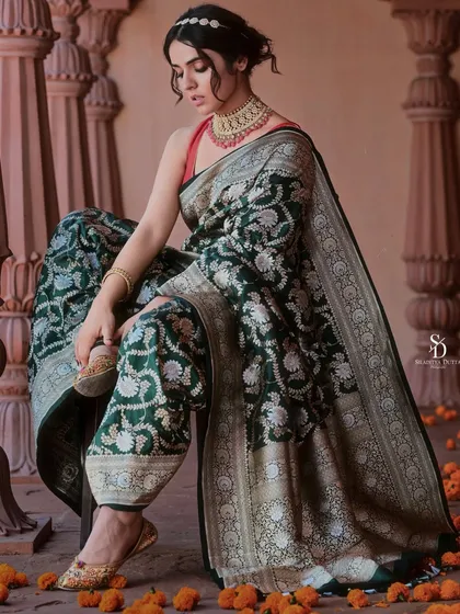 A model styled in a unique dhoti-style saree drape for a brand campaign. This shot combines traditional fabric with a modern silhouette, set against architectural pillars and scattered marigold flowers.