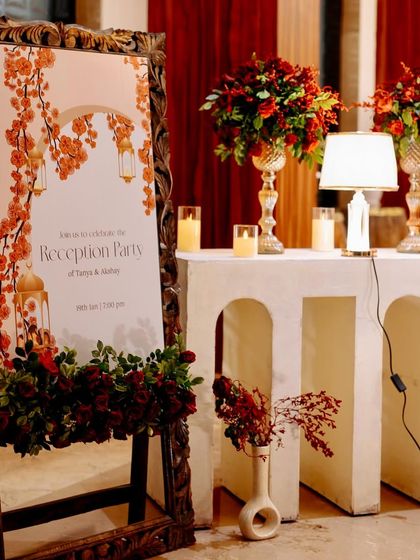 The elegant welcome sign for the reception, set in a carved wooden frame and surrounded by beautiful red floral arrangements.