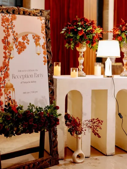 The elegant welcome sign for the reception, set in a carved wooden frame and surrounded by beautiful red floral arrangements.