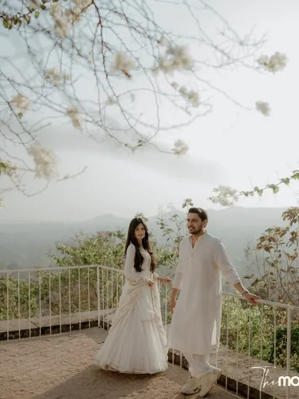 A beautiful portrait of a couple on a balcony with white flowers overhead and a hazy mountain view behind them. The image feels calm, airy, and deeply romantic.