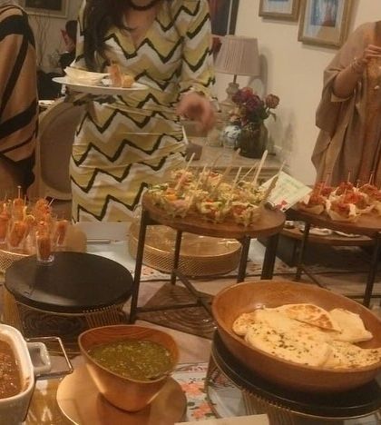 Guests enjoying a high-tea experience. The buffet includes a variety of appetizers on tiered stands, hot snacks like Mattra Kulcha, and an array of desserts.