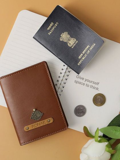 A personalized passport cover in tan vegan leather, customized for 'Ronak' with a ship charm. It's a perfect gift for someone who loves to travel.