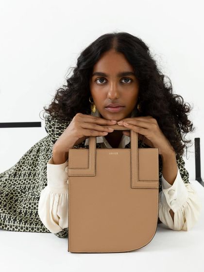 A creative composition where the model frames her face with the handbag. This is a more editorial approach to accessory photography, creating a memorable and artistic shot.